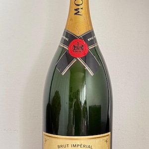 May include: A dark green glass bottle of Moët & Chandon Brut Impérial champagne. The bottle features a gold foil neck wrap with a black label, a red circular seal, and a large rectangular cream-colored label with black text and a gold crown.
