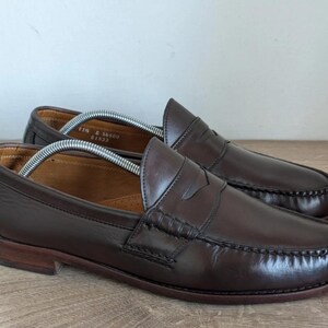 May include: A pair of brown leather penny loafers. The shoes have a classic design with a rounded toe, a strap across the vamp, and a low heel. The leather has a polished finish.