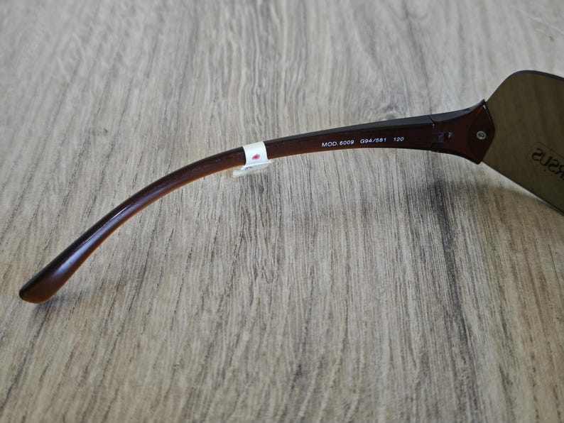 May include: Close-up of a pair of brown sunglasses with a curved arm. The text "MOD. 8009 094/S81 120" is printed on the arm. The sunglasses are on a wooden surface.