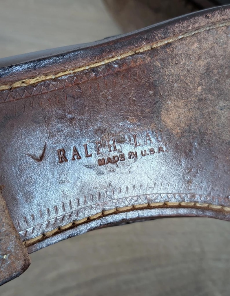 May include: Close-up of the sole of a brown leather shoe. The text "RALPH LAUREN MADE IN U.S.A." is visible. The stitching around the sole is a light tan color.