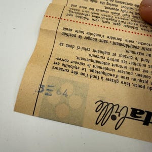K&ouml;nnte beinhalten: Ein Vintage-Papierdokument mit Text in mehreren Sprachen, darunter "Jif Waterman". Das Papier ist hellbraun mit schwarzem und rotem Text. Das Dokument ist gefaltet und eine Hand ist zu sehen, die das Papier h&auml;lt.