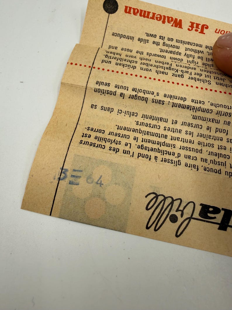 K&ouml;nnte beinhalten: Ein Vintage-Papierdokument mit Text in mehreren Sprachen, darunter "Jif Waterman". Das Papier ist hellbraun mit schwarzem und rotem Text. Das Dokument ist gefaltet und eine Hand ist zu sehen, die das Papier h&auml;lt.