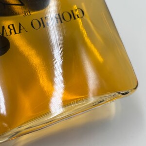 May include: A clear glass perfume bottle filled with amber-colored liquid. The bottle features black text printed on the glass that reads GIORGIO ARMANI. The design is rectangular with rounded corners and a smooth, reflective surface.