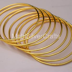 Peut inclure: Plusieurs bracelets dorés, disposés en superposition. Les bracelets sont fins et circulaires, avec une surface lisse et réfléchissante. L'image est bien éclairée, mettant en valeur l'éclat métallique des bijoux.
