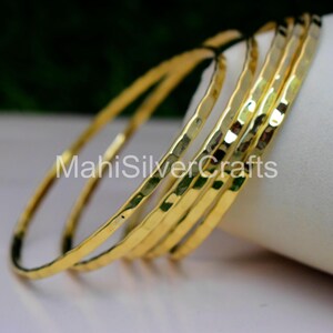 Peut inclure: Ensemble de bracelets dorés avec une texture martelée. Les bracelets sont empilés, mettant en valeur leur forme circulaire et leur surface réfléchissante. Le texte "MahiSilverCrafts" est visible sur l'image.