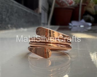 May include: A copper-colored, spiral-shaped ring. The ring has a smooth, polished finish and a unique design. The text "MahiSilverCrafts" is visible on the ring. The ring appears to be made of metal and is likely a piece of jewelry.