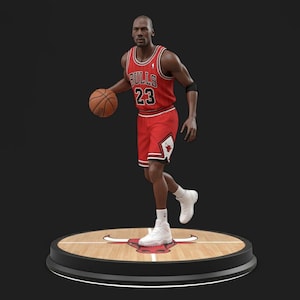 Puede incluir: Figura de un jugador de baloncesto con uniforme rojo y negro con el número 23. La figura sostiene un balón de baloncesto y está de pie sobre una plataforma redonda con diseño de cancha de baloncesto.