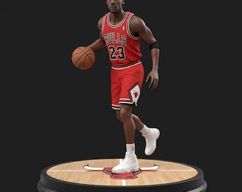May include: A figurine of a basketball player in a red and black uniform with the number 23. The figure is holding a basketball and is standing on a round platform with a basketball court design.