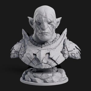 Pode incluir: Um busto cinza-claro de um personagem orc de fantasia com orelhas pontudas, expressão facial severa e placas de armadura texturizadas sobre os ombros e peito. A figura está montada sobre uma base de formações rochosas irregulares.