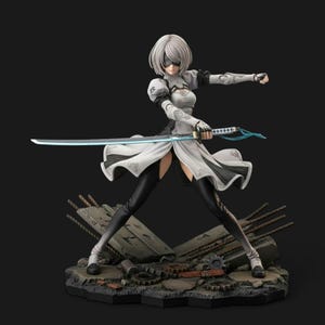 May include: A detailed figurine of a female character in a white and black outfit, holding a glowing blue sword. The figure has short, silver hair and a blindfold. The base is a detailed diorama of rubble and mechanical parts.