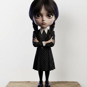 May include: A doll of a young girl with black pigtails, wearing a black polka dot dress with a white collar and cuffs, black tights, and black shoes. The doll is standing on a wooden shelf against a white background.