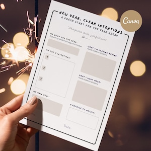 May include: A white and beige New Year's intentions planner with the text "New Year, Clear Intentions" and "Progress over perfection". The planner includes sections for intentions, goals, and promises. Sparklers are in the background.
