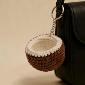 May include: A crocheted coconut keyring with a brown exterior and white interior, attached to a silver chain and a black handbag. The keyring is a handmade accessory.