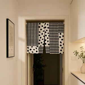 May include: A doorway curtain with a black and white pattern. The curtain is divided into three sections: a vertical striped pattern, a polka dot pattern, and a checkered pattern. The curtain hangs in a white doorway.