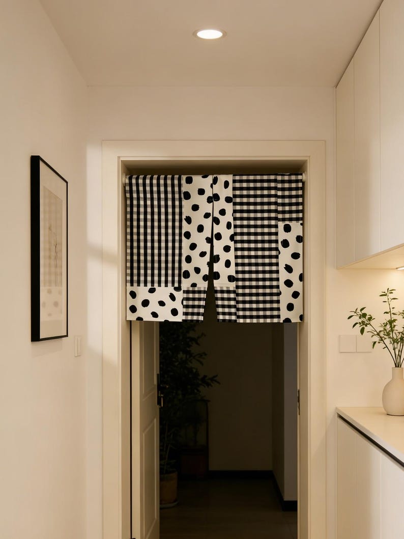 May include: A doorway curtain with a black and white pattern. The curtain is divided into three sections: a vertical striped pattern, a polka dot pattern, and a checkered pattern. The curtain hangs in a white doorway.