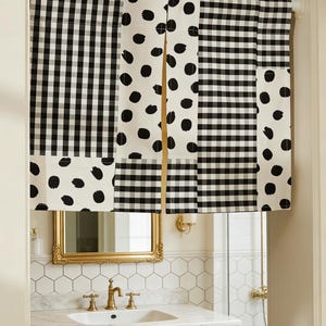 May include: Black and white patterned window valance. The valance features a patchwork design with alternating sections of gingham check and large black polka dots on a white background. The valance is installed above a bathroom sink with a gold-framed mirror.
