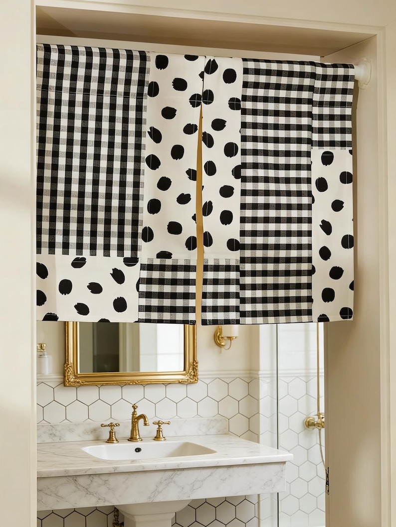 May include: Black and white patterned window valance. The valance features a patchwork design with alternating sections of gingham check and large black polka dots on a white background. The valance is installed above a bathroom sink with a gold-framed mirror.