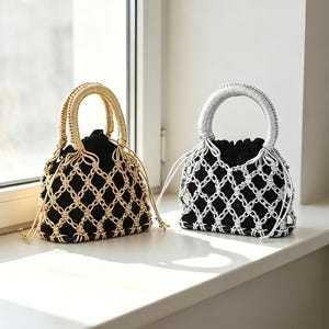 以下が含まれることがあります： 黒い布製の巾着袋を、結び目のある装飾的なコードで覆った小さなハンドバッグ2点。片方はメタリックゴールドのコードとハンドル、もう片方はメタリックシルバーのコードとハンドルで構成されており、どちらも巾着型の開口部を備えています。