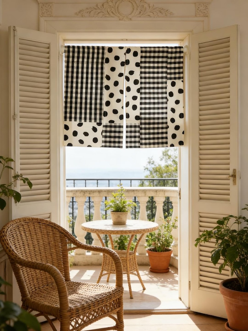 May include: A bright, airy balcony scene with a woven chair, small round table, and potted plants. The focal point is a window with a patchwork valance featuring black and white polka dot and gingham patterns. White shutters frame the view.