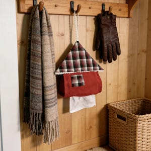 May include: A wooden wall-mounted shelf with hooks displays a fringed scarf, a house-shaped tissue holder, and leather gloves. A woven basket and a faux fur rug sit below. The tissue holder is red with a plaid roof.