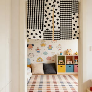 May include: A doorway curtain with a patchwork design of black and white polka dots and gingham patterns. The curtain hangs in front of a room with a colorful rug, wall decals, and storage cubes, creating a playful atmosphere.