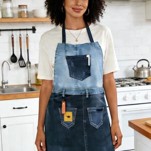 Pode incluir: Avental de ganga de duas cores, com uma secção superior azul clara e uma saia azul escura. O avental tem um bolso no peito e dois bolsos na saia. Uma pequena etiqueta de couro com um quadrado amarelo e uma estrela preta pende do avental.