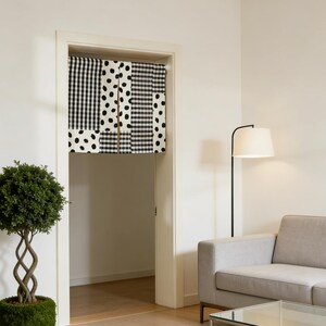 May include: A doorway curtain with a patchwork design of black and white patterns, including gingham, polka dots, and stripes. The curtain hangs in a white doorway, with a glimpse of a room beyond. The room features a sofa, a floor lamp, and a geometric rug.