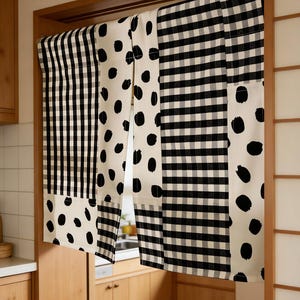 May include: A decorative kitchen curtain with a patchwork design. The curtain features alternating panels of black and white gingham, black polka dots on a cream background, and vertical black stripes. The curtain hangs in a wooden doorway.