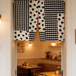May include: A black and white patterned door curtain. The curtain features a patchwork design with gingham and polka dot patterns. The curtain hangs in a doorway, with a restaurant visible in the background.