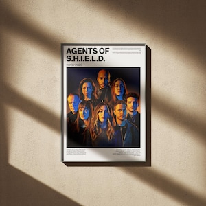 May include: A framed poster featuring the cast of "Agents of S.H.I.E.L.D." The poster has a white border and the title "AGENTS OF S.H.I.E.L.D." is at the top. The poster's background is a beige wall with shadows.