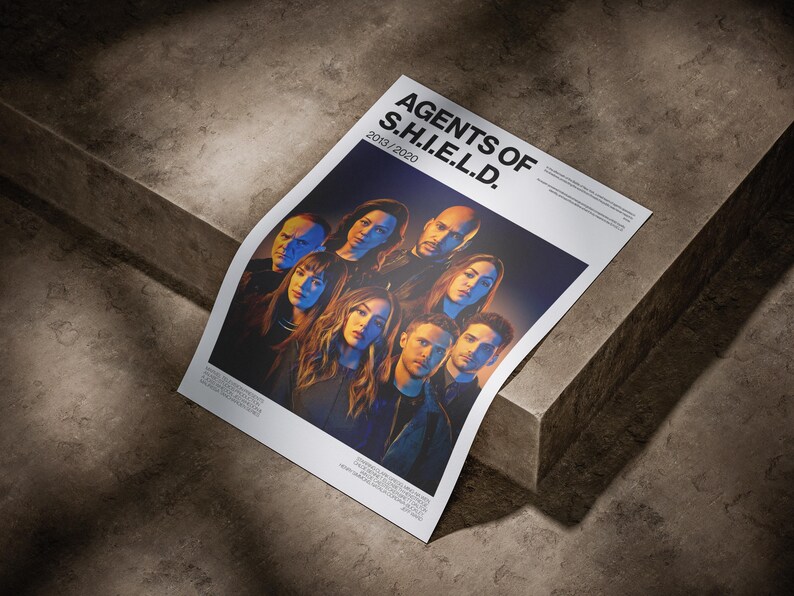 May include: A poster featuring the cast of "Agents of S.H.I.E.L.D." against a dark background. The poster has the show's title and the years 2013/2020 printed in white. The image is on a white background and is resting on a concrete surface.