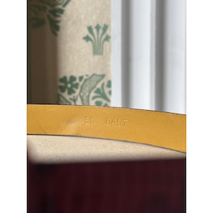 May include: Close-up of a yellow leather belt. The belt's underside displays the stamped numbers "5C 0497". The background includes a patterned fabric and a white curtain, providing a neutral backdrop for the belt's details.