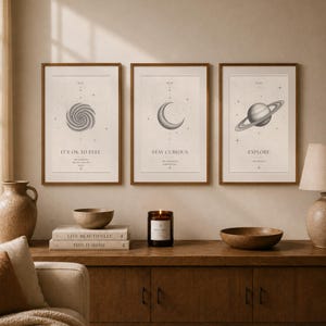 Pode incluir: Três impressões artísticas emolduradas com molduras de madeira castanha. As impressões apresentam uma galáxia espiral, uma lua crescente e Saturno. Cada impressão tem uma citação: "It's ok to feel", "Stay Curious" e "Explore".