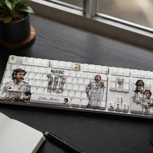 May include: A white mechanical keyboard featuring custom keycaps with printed graphics of Luka Modrić in a Real Madrid kit, the number 10, the text "MODRIC" and "Luka Modrić," and a Champions League trophy icon across several keys.