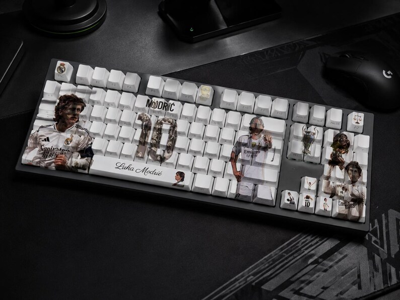 May include: A black mechanical keyboard with white keycaps featuring custom graphics of Luka Modrić, the number 10, and Real Madrid imagery. The spacebar displays the text Luka Modrić, while other keys show various player portraits and trophies.