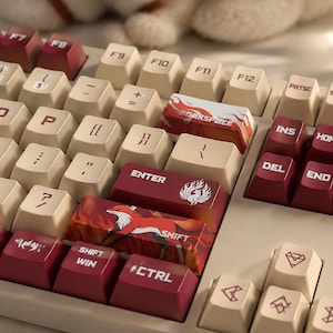 May include: Close-up of a mechanical keyboard with cream-colored keycaps and burgundy accent keys. The keyboard features custom keycaps with a fox and flame design. The keys include "SHIFT", "CTRL", and "ENTER".