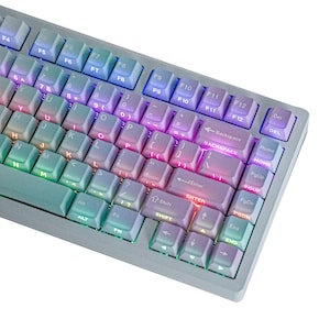 May include: A mechanical keyboard featuring a gradient color scheme that transitions from light blue to purple across the keycaps. The keys are backlit with integrated RGB lighting, and the layout includes standard alphanumeric keys, function keys, and navigation keys.