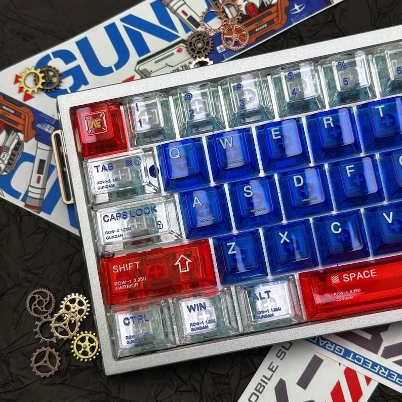 May include: A silver mechanical keyboard with red, clear, and blue keycaps. The keycaps are arranged in a standard QWERTY layout. The keyboard has a metal frame and includes decorative gears and text that reads "GUN".