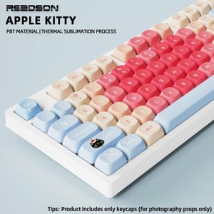 May include: A white keyboard with light blue, beige, and red keycaps. The keyboard has the text "APPLE KITTY" and "PBT MATERIAL | THERMAL SUBLIMATION PROCESS". The keycaps are arranged in a standard QWERTY layout.