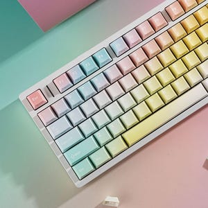 May include: A white mechanical keyboard with gradient keycaps in pastel colors, including pink, blue, and yellow. The keyboard has a standard layout with function keys and a numeric keypad. The Esc key is pink.