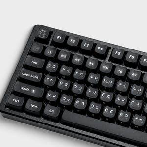 May include: A black computer keyboard featuring custom keycaps with white printed cat-themed facial expressions and icons. The keys display various eyes, mouths, and cat silhouettes, replacing standard letter and number characters with playful designs.