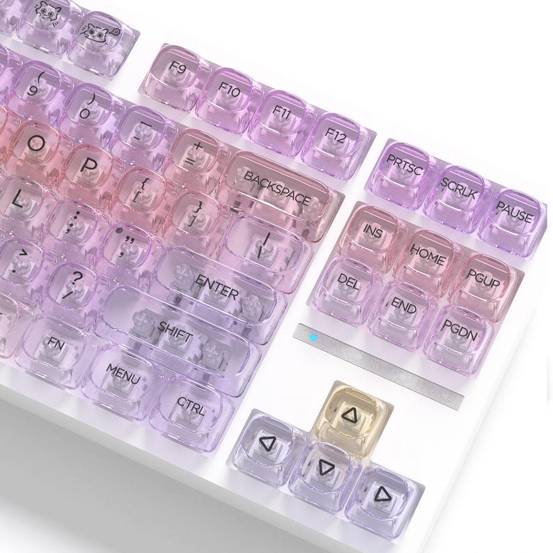 May include: A close-up of a white keyboard with transparent keycaps. The keycaps have a gradient of pink and purple hues. The keys are labeled with white text, including function keys, letters, and symbols. Some keycaps have small cartoon cat designs.