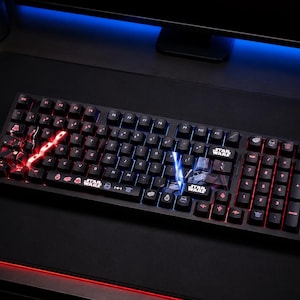 May include: A black mechanical computer keyboard featuring Star Wars themed keycaps with red and blue LED backlighting. The keys display various Star Wars icons and the Star Wars logo, with specific keys illuminated in bright red and blue light.