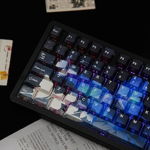 May include: A black mechanical keyboard featuring custom keycaps with a blue and white abstract pattern. The keys display standard QWERTY lettering and symbols, with integrated RGB backlighting illuminating the spaces between the keys.