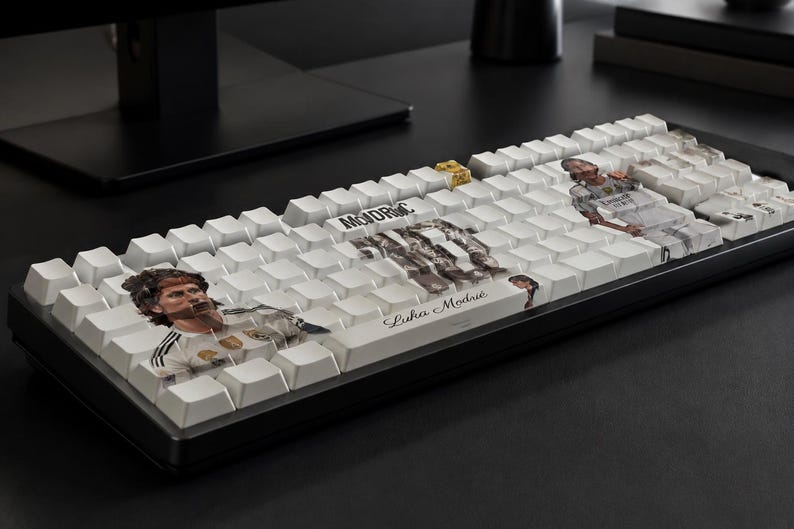 May include: A black computer keyboard with white keycaps featuring custom graphics of a soccer player. The keys display the name Luka Modrić in script, the text MODRIC in block letters, and multiple photographic images of the athlete in a white jersey.