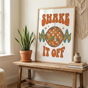 May include: A framed print with the words "SHAKE IT OFF" in orange, with a disco ball illustration. The print is displayed on a wooden bench with a potted plant and decorative items. The style is retro.