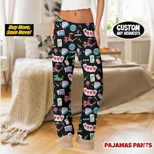 May include: Black pajama pants with a repeating pattern of Asian-themed illustrations in pink, blue, and green. The pants have a drawstring waist and the words "Custom Any Requests" are printed on the right leg. The words "Buy More, Save More!" are printed on the left leg.