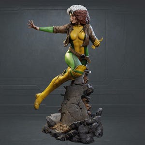 May include: A detailed statue of Rogue from the X-Men. She is depicted in a dynamic pose, wearing a yellow and green bodysuit, brown jacket, and boots. Her hair is brown with white streaks. The statue is mounted on a rocky base.