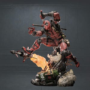 Puede incluir: Estatua dinámica de Deadpool con traje rojo y negro, en plena acción con espada y pistola. La figura está sobre una base detallada con un cohete, llamas y una caja de municiones verde. Diseño muy detallado.