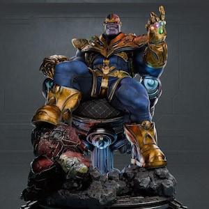 May include: A detailed statue of Thanos, a purple-skinned character, seated on a throne. He wears blue and gold armor, with the Infinity Gauntlet on his right hand. The statue is set on a rocky base.